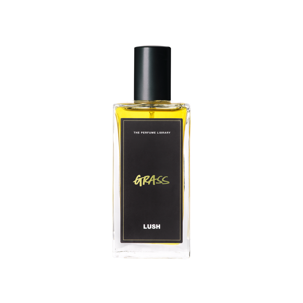 A glass perfume bottle filled with canary yellow liquid. A black label reads 'The Perfume Library' and 'Grass'.